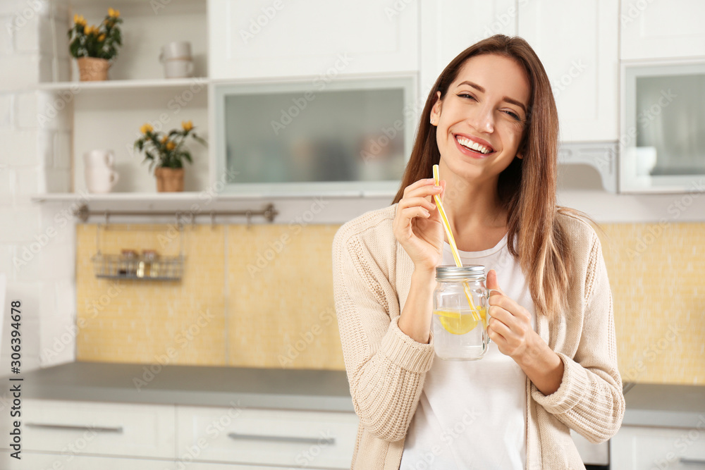 Young woman with mason jar of lemon water in kitchen Young woman with mason jar of lemon water in kitchen