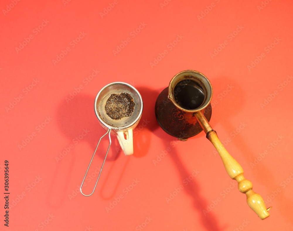 Copper cezva with cooked coffee and cup with strainer on red background Copper cezva with cooked coffee and cup with strainer on red background