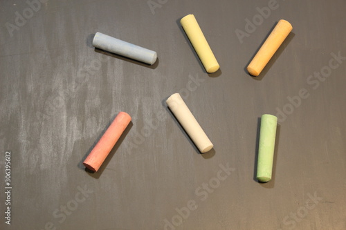 Colorful cylinder chalk sticks on dark grey board with some pics and lines