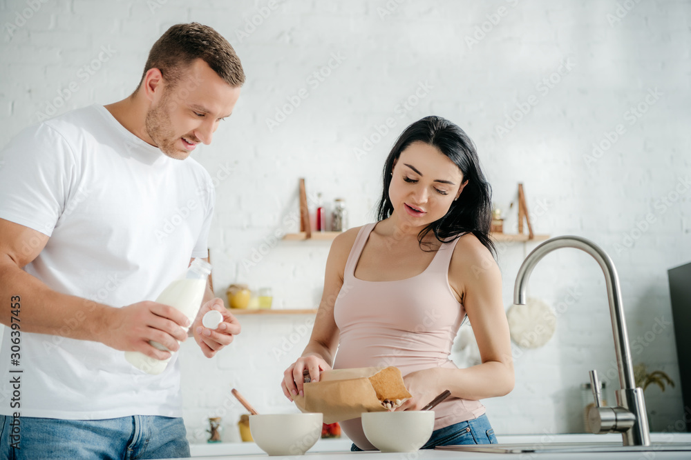 happy pregnant couple making cereals with milk in kitchen happy pregnant couple making cereals with milk in kitchen