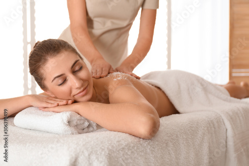 Young woman having body scrubbing procedure with sea salt in spa salon