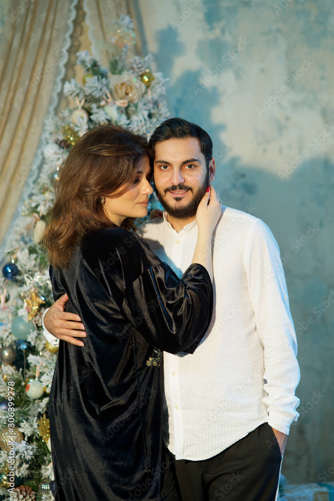 Young beautiful couple in love stands in a room decorated for the new year. Young beautiful couple in love stands in a room decorated for the new year.