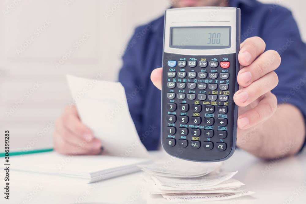 Person with bills and a calculator calculates the family budget, shows on the calculator the amount of 300, male hands, cropped image, close up, toned Person with bills and a calculator calculates the family budget, shows on the calculator the amount of 300, male hands, cropped image, close up, toned
