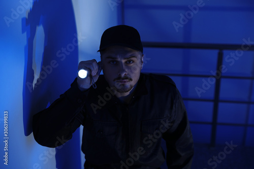 Male security guard with flashlight in dark room