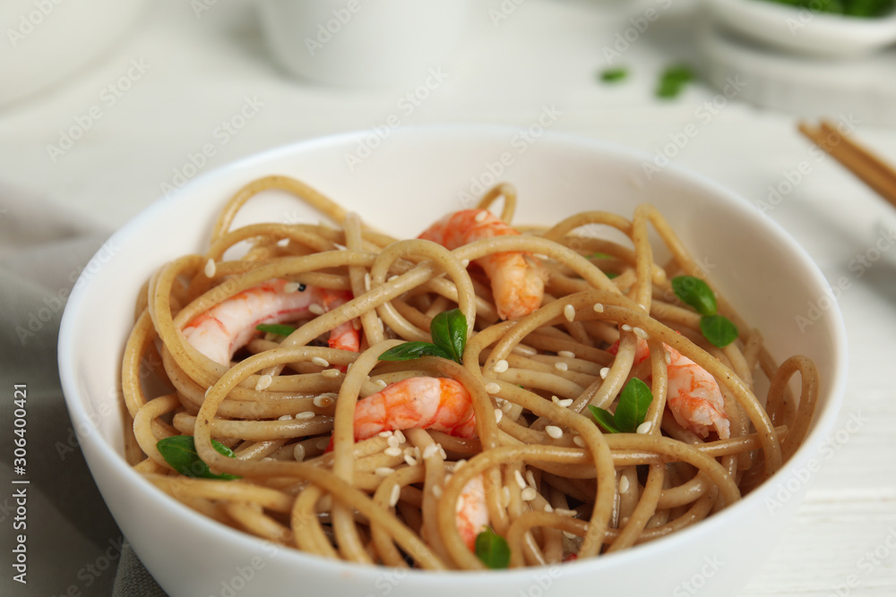 Tasty buckwheat noodles with shrimps in bowl on white wooden table, closeup