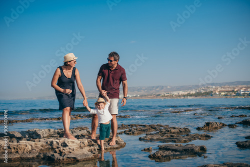 Family with a child stand on the stones against the background of the sea. © Anna