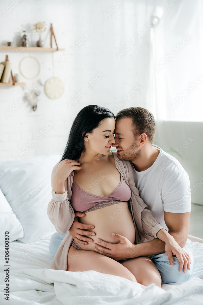 happy husband hugging his attractive pregnant wife in bed happy husband hugging his attractive pregnant wife in bed