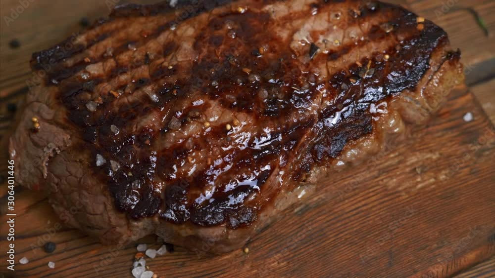 Grilling Beef Steak with Spices on the Rustic Cutting Board on Wooden Background. Cooking Roasted Rib Eye Meat on the Table Grilling Beef Steak with Spices on the Rustic Cutting Board on Wooden Background. Cooking Roasted Rib Eye Meat on the Table