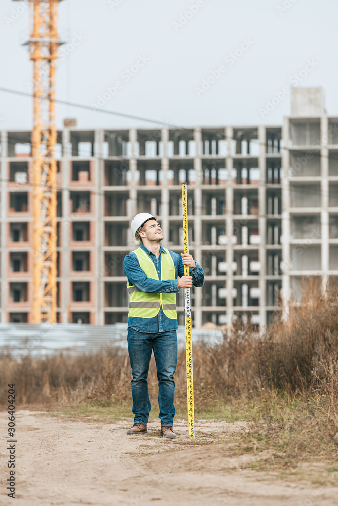 Smiling surveyor holding ruler with construction site at background
