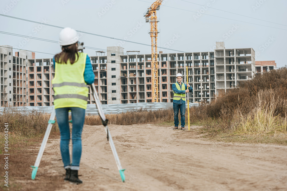 Surveyors measuring land on dirt road with construction site at background Surveyors measuring land on dirt road with construction site at background
