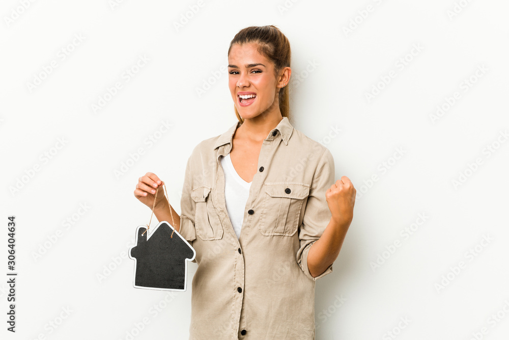 Young caucasian woman holding a house icon cheering carefree and excited. Victory concept. Young caucasian woman holding a house icon cheering carefree and excited. Victory concept.