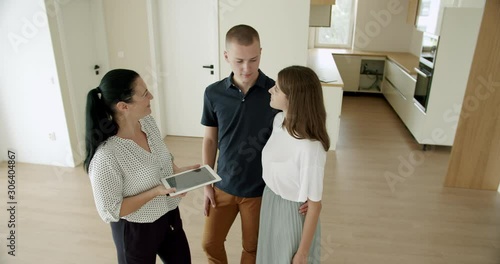 Estate agent using digital tablet with young couple in new house. Estate agent showing young couple around a new house with digital tablet.