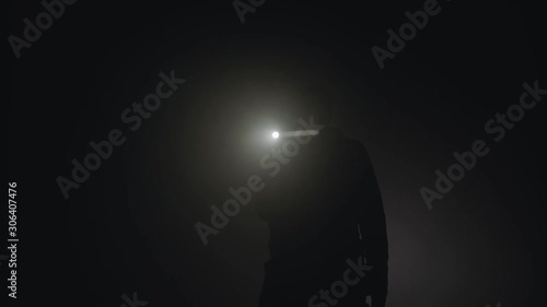 Silhouette of man shining with flashlight in the dark. Stock footage. Silhouette of man in thick fog photo