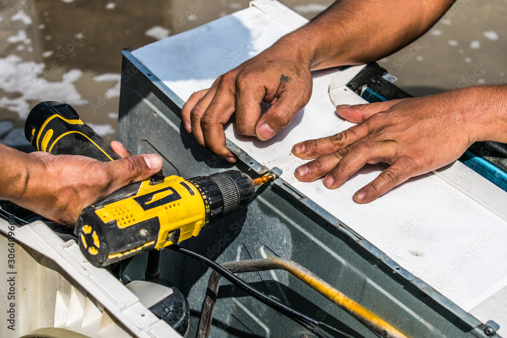 a professional electrician man is fixing the screw by auto screw driver machine into the window air conditioner after the cleaning a professional electrician man is fixing the screw by auto screw driver machine into the window air conditioner after the cleaning