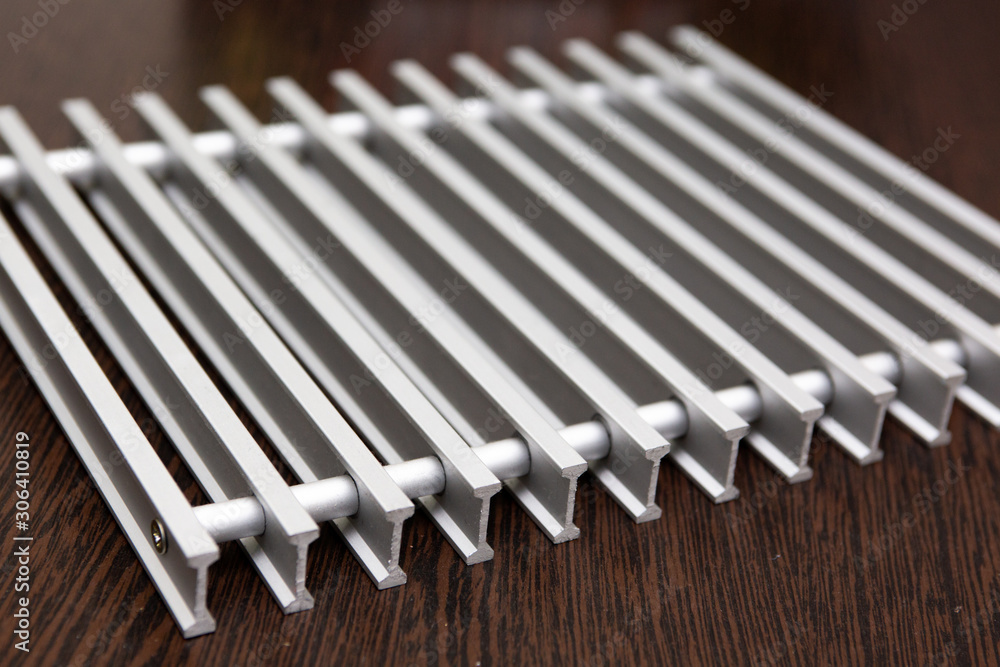 On a dark table lies a lattice of silver metal strips connected by inserts. On a dark table lies a lattice of silver metal strips connected by inserts.