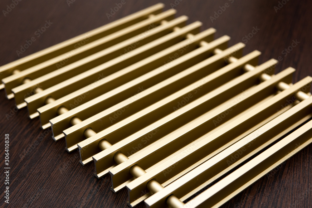 On a dark table lies a lattice of gold-plated metal strips connected by inserts. On a dark table lies a lattice of gold-plated metal strips connected by inserts.