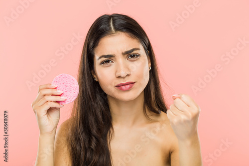 Young indian woman holding a facial skin care disc showing fist to camera, aggressive facial expression.