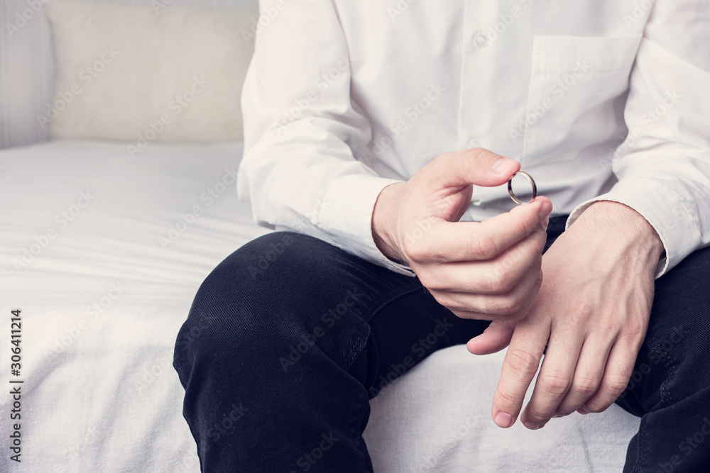 Concept of divorce and family disintegration. Man with wedding ring sitting in a marital bedroom, close up, cropped image, toned