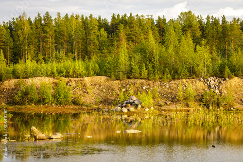 Forest lake, mound of boulders and deciduous forest on the background. Summer landscape.