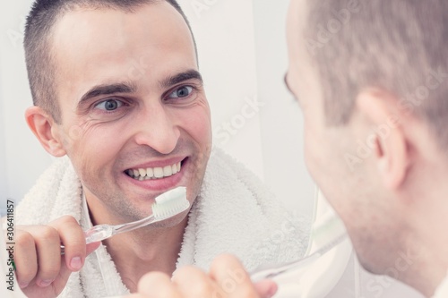 Handsome man brushing teeth and looking to mirror, portrait, toned