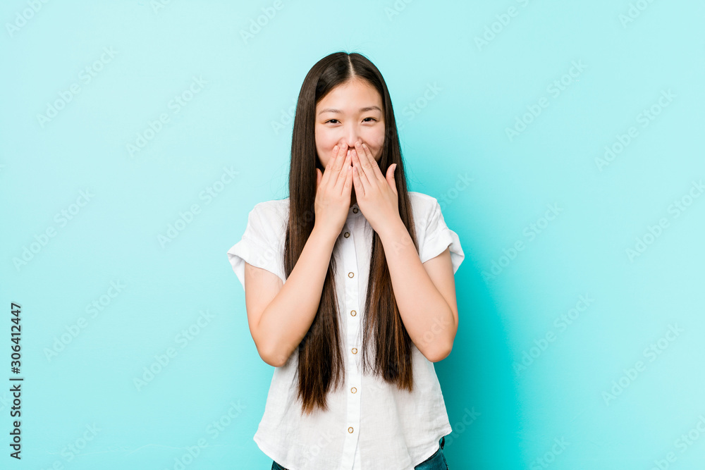 Young pretty chinese woman laughing about something, covering mouth with hands.