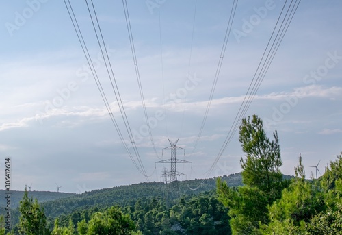 Electric pylons placed at a forest photographed on a sunny day with blue sky.