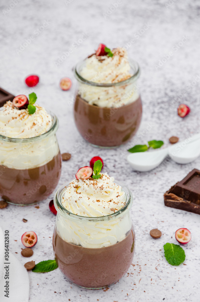Chocolate cream (pudding, jelly, panna cotta) on agar agar with whipped cream on top in glass jars on a light stone background. Chocolate cream (pudding, jelly, panna cotta) on agar agar with whipped cream on top in glass jars on a light stone background.