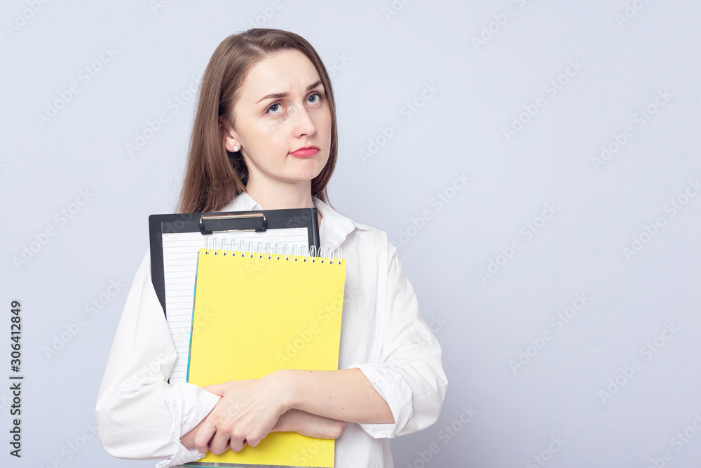 Discontented girl student with notebooks. Concept of education. Portrait, grey background, copy space, slogan, toned Discontented girl student with notebooks. Concept of education. Portrait, grey background, copy space, slogan, toned
