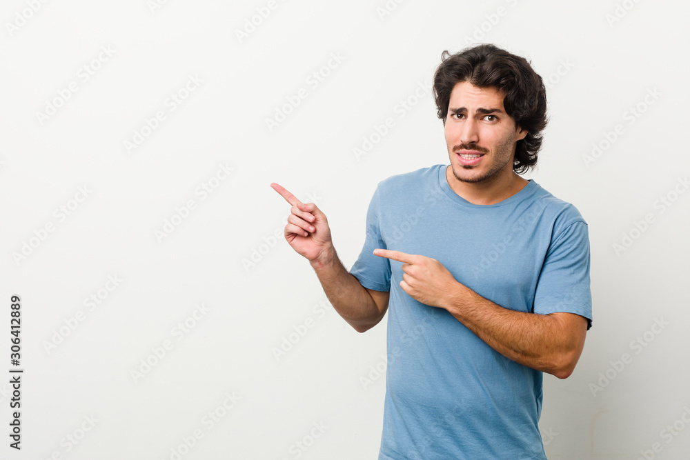 Young handsome man against a white background shocked pointing with index fingers to a copy space. Young handsome man against a white background shocked pointing with index fingers to a copy space.
