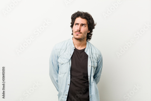 Young handsome man against a white background confused, feels doubtful and unsure.