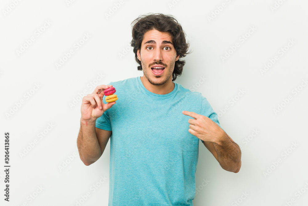 Young man holding macaroons surprised pointing at himself, smiling broadly. Young man holding macaroons surprised pointing at himself, smiling broadly.