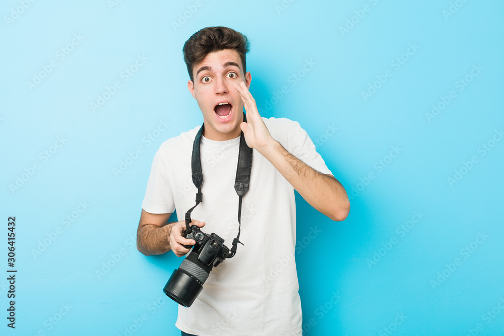 Young caucasian photographer man holding a camera shouting excited to front. Young caucasian photographer man holding a camera shouting excited to front.
