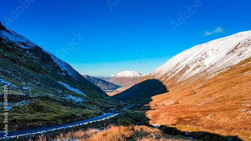 Kirkstone Pass in autumn with snow capped peaks in the Lake District, Cumbria, UK. Beautiful sunny day with blue sky overlooking the touristic road in the valley that connects with Ullswater.