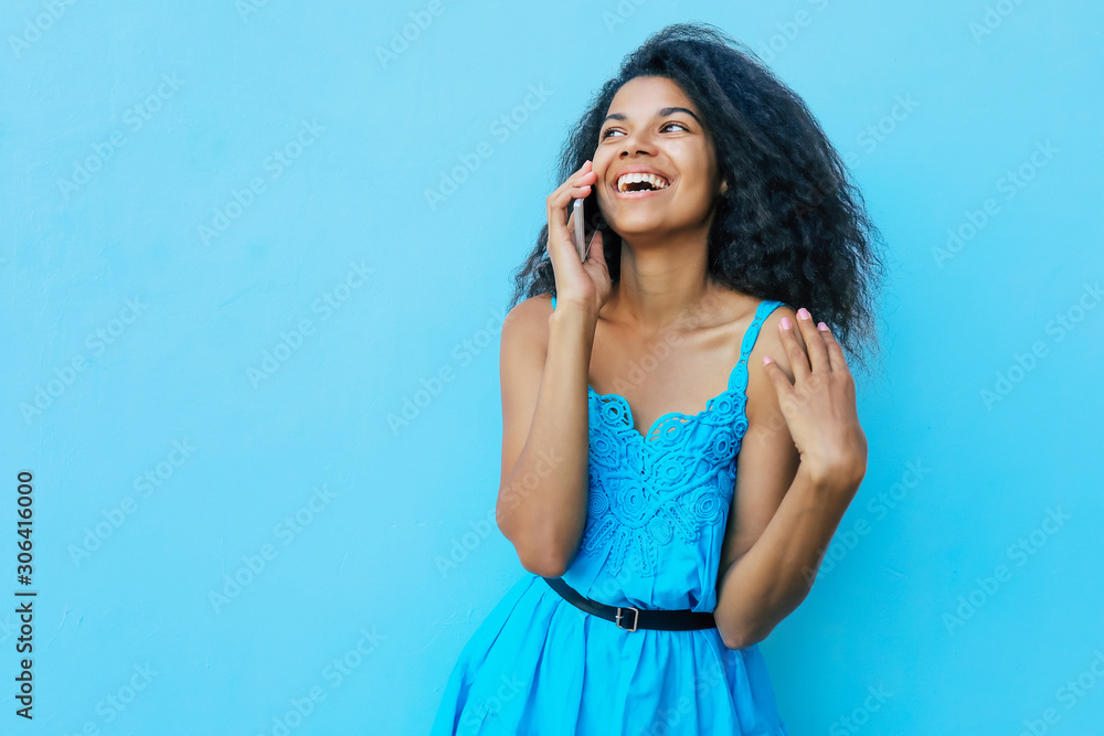 Fototapeta premium Greatness. Front portrait of a joyful African American girl with shoulder-length messy black hair, who is laughing sincerely while talking on the phone and looking to the left.