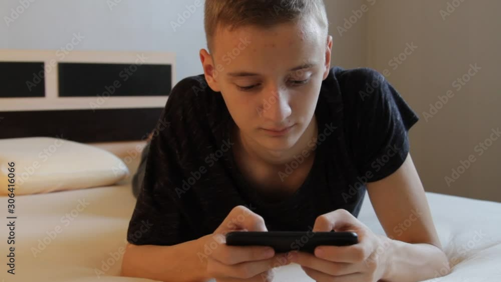 Close-up portrait of young teenager boy texting messages and playng a game using his phone Close-up portrait of young teenager boy texting messages and playng a game using his phone