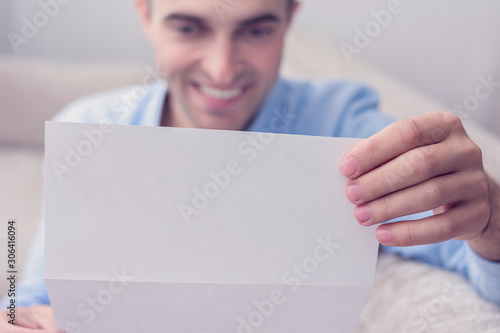 Happy man reading a letter, guy sitting on the couch, cropped image, copy space, toned