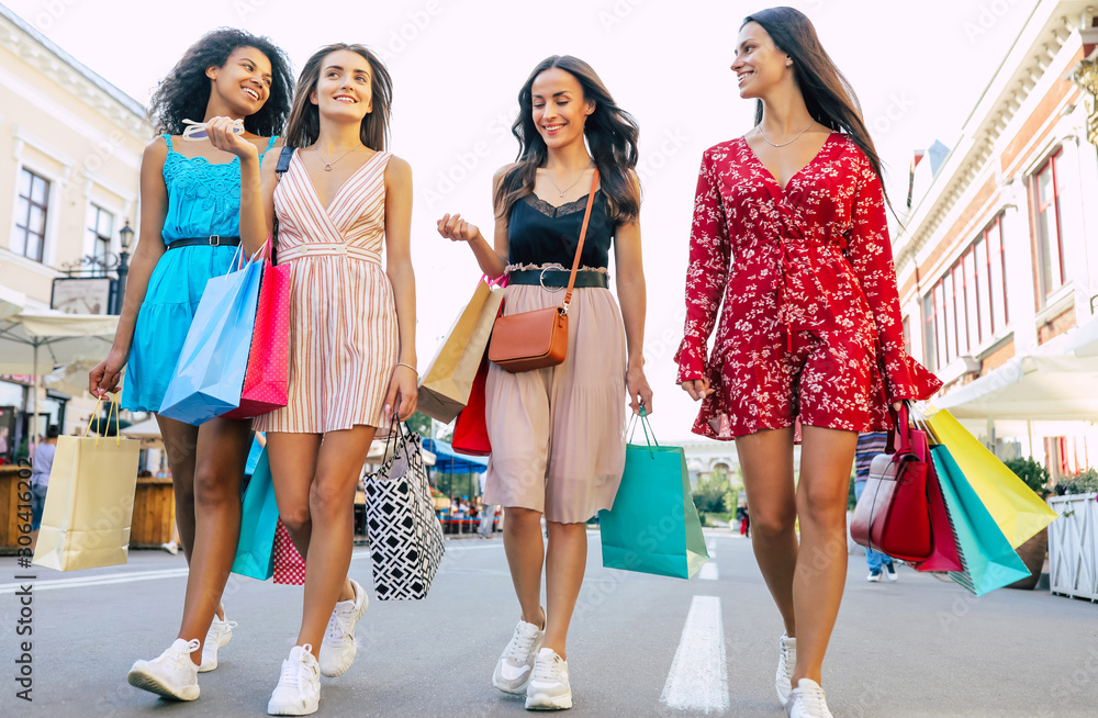 Perfect weekends. Low-angled photo of four beautiful women in summer dresses, walking towards the camera in the city center with their purchases from the mall. Perfect weekends. Low-angled photo of four beautiful women in summer dresses, walking towards the camera in the city center with their purchases from the mall.