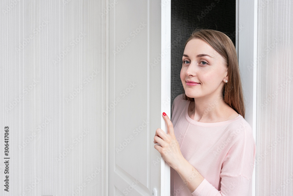 Young woman spying on the door, portrait, copy space, toned Young woman spying on the door, portrait, copy space, toned