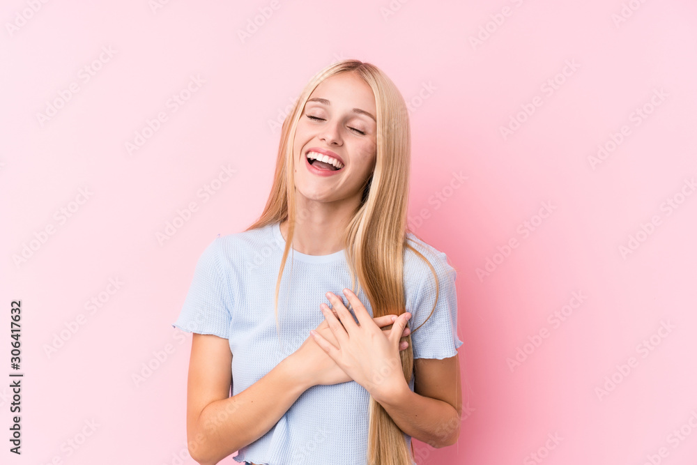 Young blonde woman on pink background laughing keeping hands on heart, concept of happiness. Young blonde woman on pink background laughing keeping hands on heart, concept of happiness.