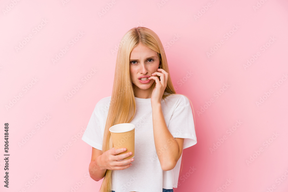 Young blonde girl holding a takeaway coffee biting fingernails, nervous and very anxious. Young blonde girl holding a takeaway coffee biting fingernails, nervous and very anxious.