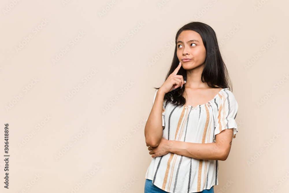 Young cute chinese teenager Young blonde woman wearing a coat against a pink background looking sideways with doubtful and skeptical expression. Young cute chinese teenager Young blonde woman wearing a coat against a pink background looking sideways with doubtful and skeptical expression.