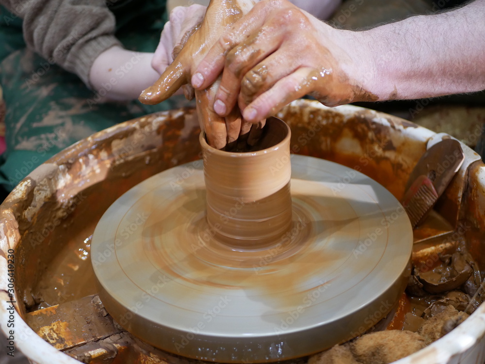The master Potter teaches the child to make a clay jug on a modern Potter's wheel with an electric drive. The hands of a child and an adult man are stained with clay. Teaching pottery.