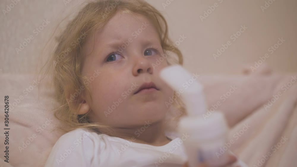 upset little girl with blue eyes undergoes procedure with modern inhaler on soft bed close view upset little girl with blue eyes undergoes procedure with modern inhaler on soft bed close view