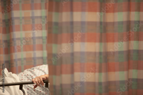 Midsection of patient holding onto bed railing lying behind curtains at hospital ward