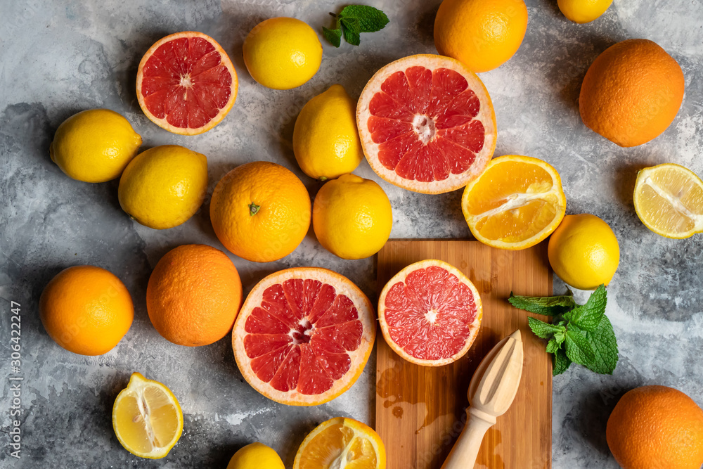 Top view on fresh citrus fruits composition with oranges, lemons, grapefruits and mint, grey background with wooden cutting board and squeezer or hand press