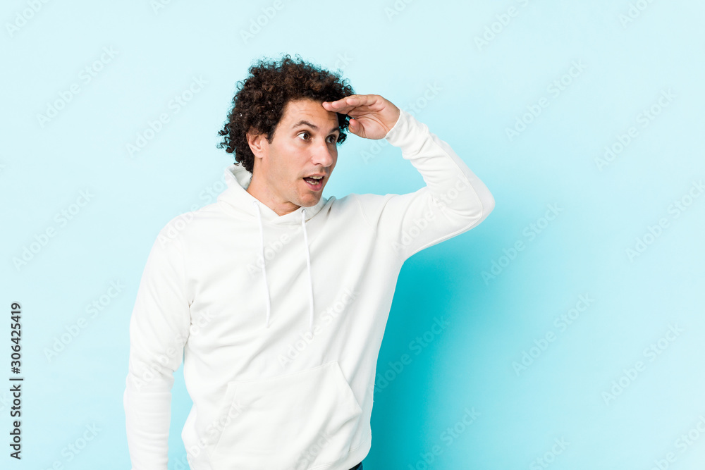Young sporty man against a blue background looking far away keeping hand on forehead. Young sporty man against a blue background looking far away keeping hand on forehead.