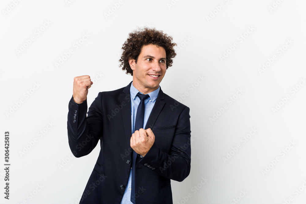 Young business curly man against white background raising fist after a victory, winner concept. Young business curly man against white background raising fist after a victory, winner concept.