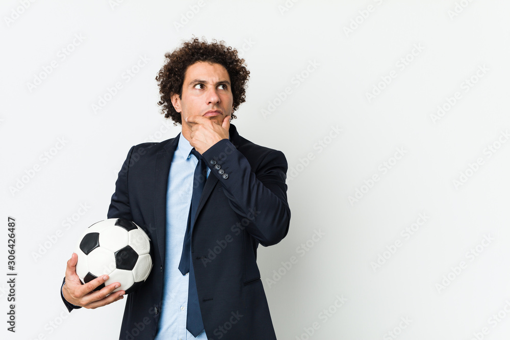 Soccer trainer holding a ball looking sideways with doubtful and skeptical expression. Soccer trainer holding a ball looking sideways with doubtful and skeptical expression.