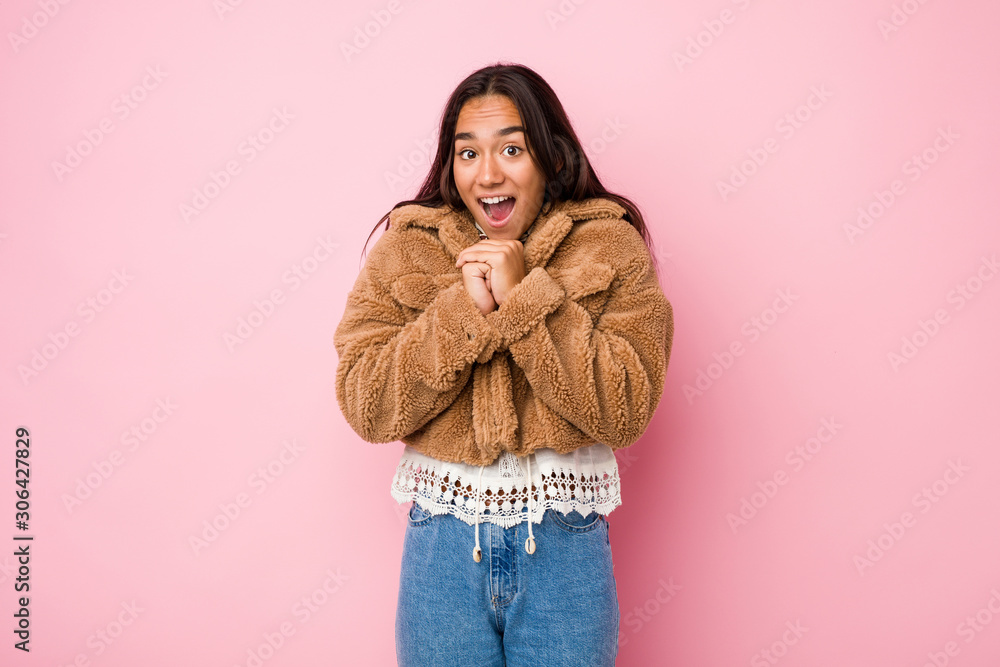 Young mixed race indian woman wearing a short sheepskin coatpraying for luck, amazed and opening mouth looking to front. Young mixed race indian woman wearing a short sheepskin coatpraying for luck, amazed and opening mouth looking to front.