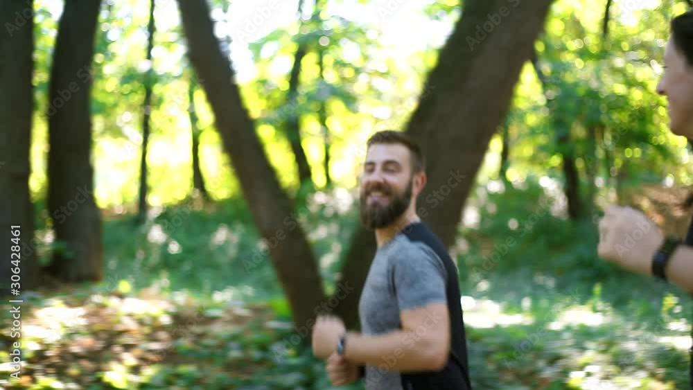 Sporty couple running on forest path, man looking on smartwatch Sporty couple running on forest path, man looking on smartwatch